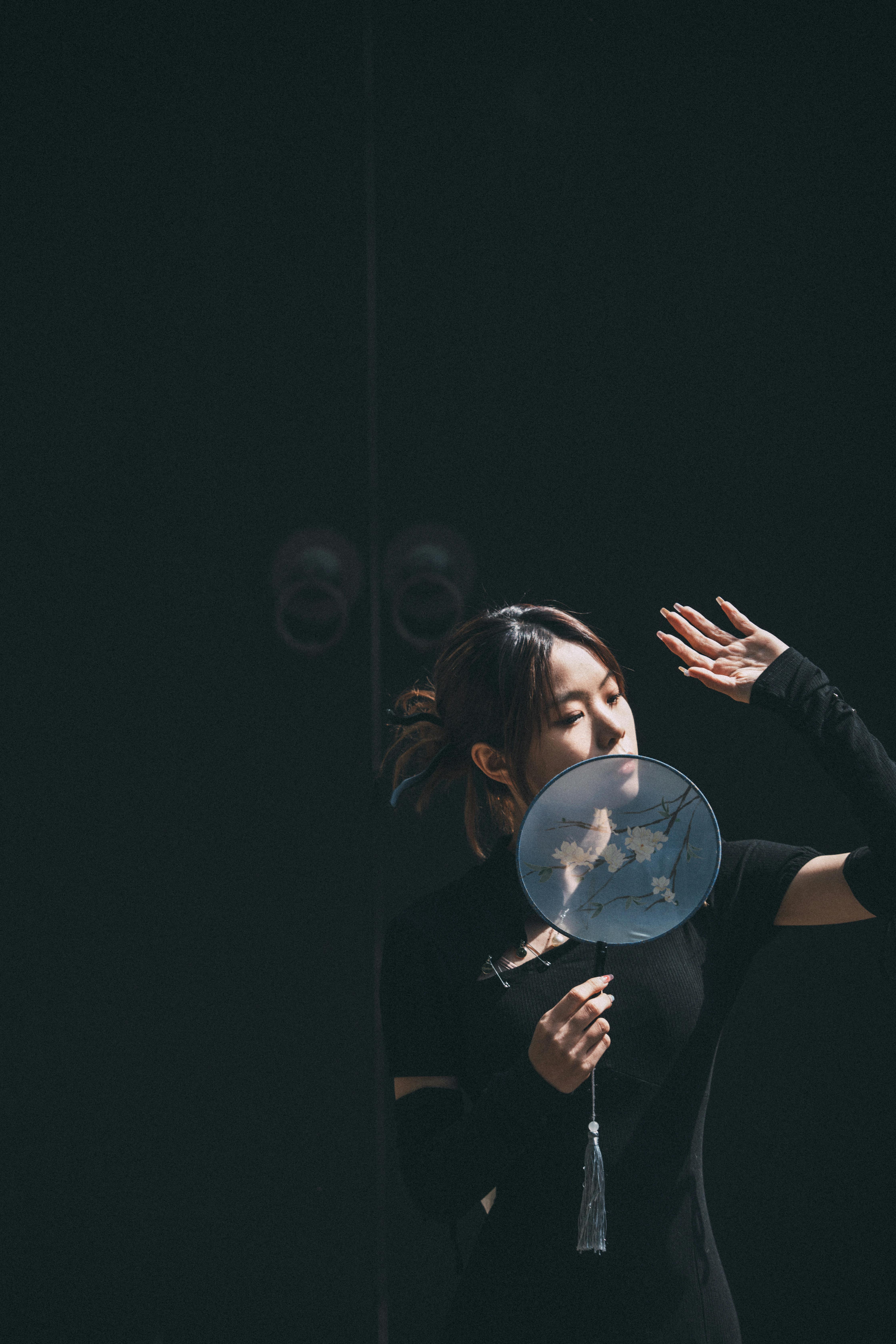 Stylish portrait of a woman in black holding a hand fan, showcasing elegance and fashion.
