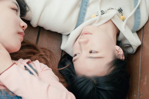 Free Two young women sharing a quiet, intimate moment lying side by side on a wooden surface. Stock Photo