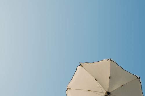 Free White beach umbrella against a clear blue sky, symbolizing summer and relaxation. Stock Photo