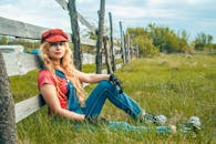 一位金发女子身着休闲装，坐在乡村的篱笆旁