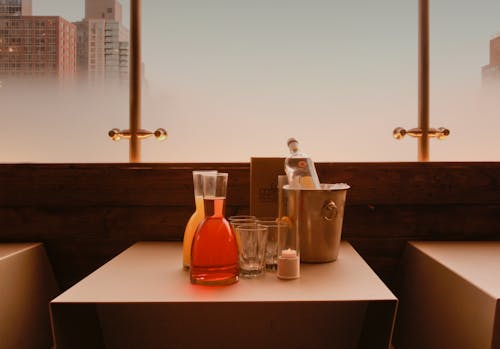 Juice, Glasses and an Ice Bucket with a Bottle of Alcohol Standing on a Table 