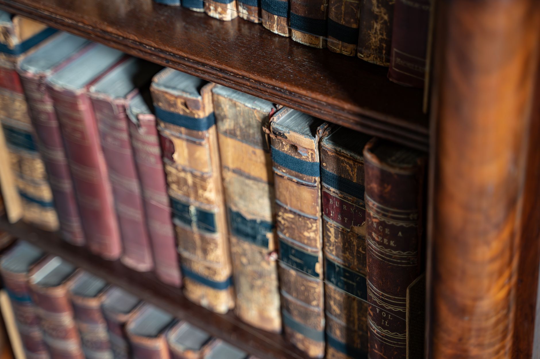 Close-up of vintage leather-bound books on rustic wooden shelves with warm lighting.