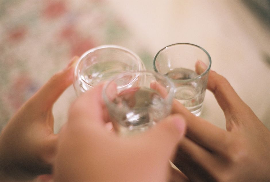 Three people clink glasses in a celebratory toast, highlighting a close-up view of hands and drinks.