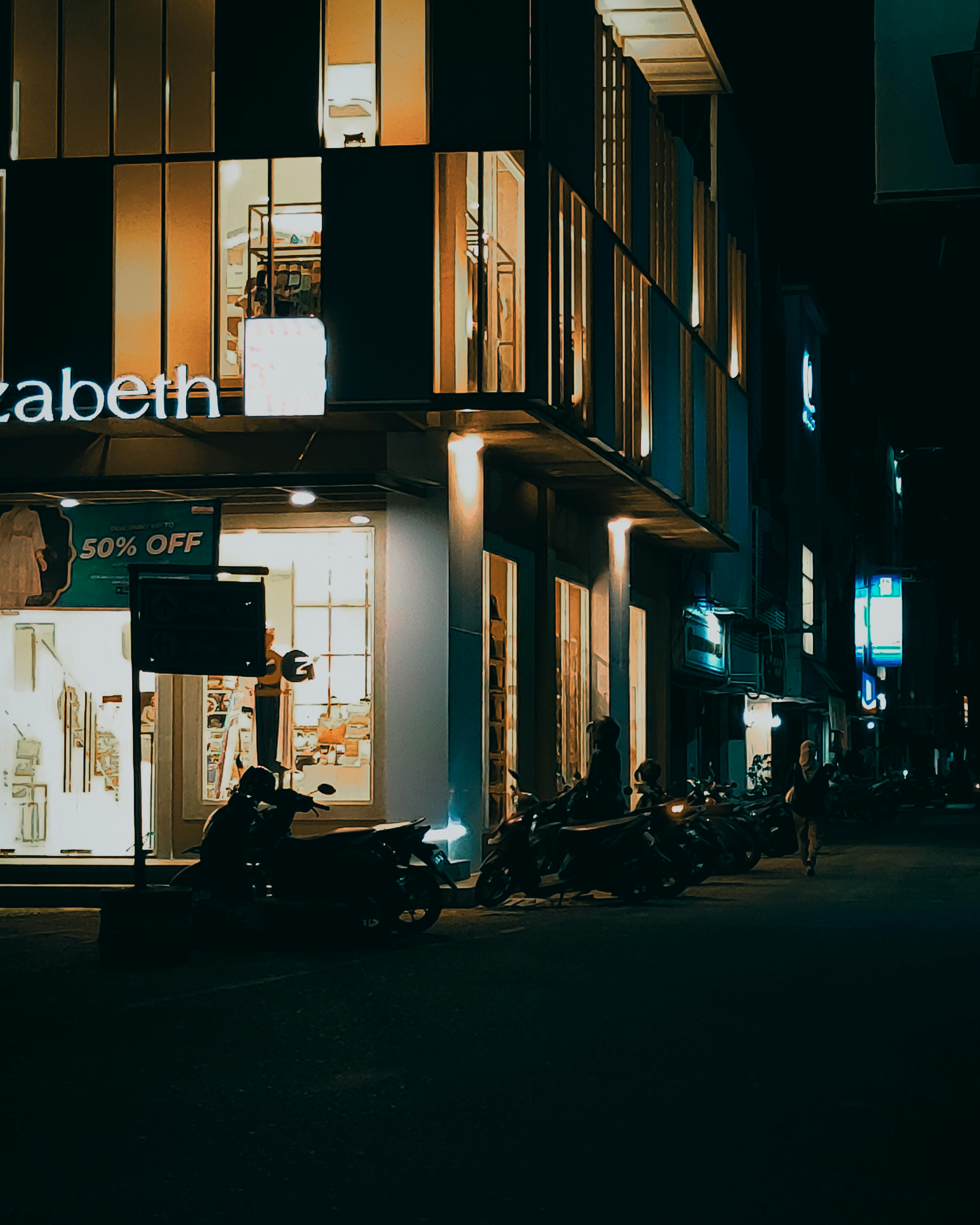 view of an illuminated building and parked motorbikes in city at night