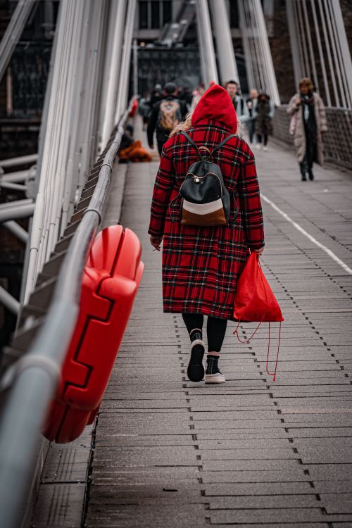 Free A person in a red coat walks on a modern footbridge in London, capturing urban life. Stock Photo