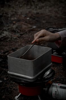 Close-up of a hand stirring food on a portable stove during camping.