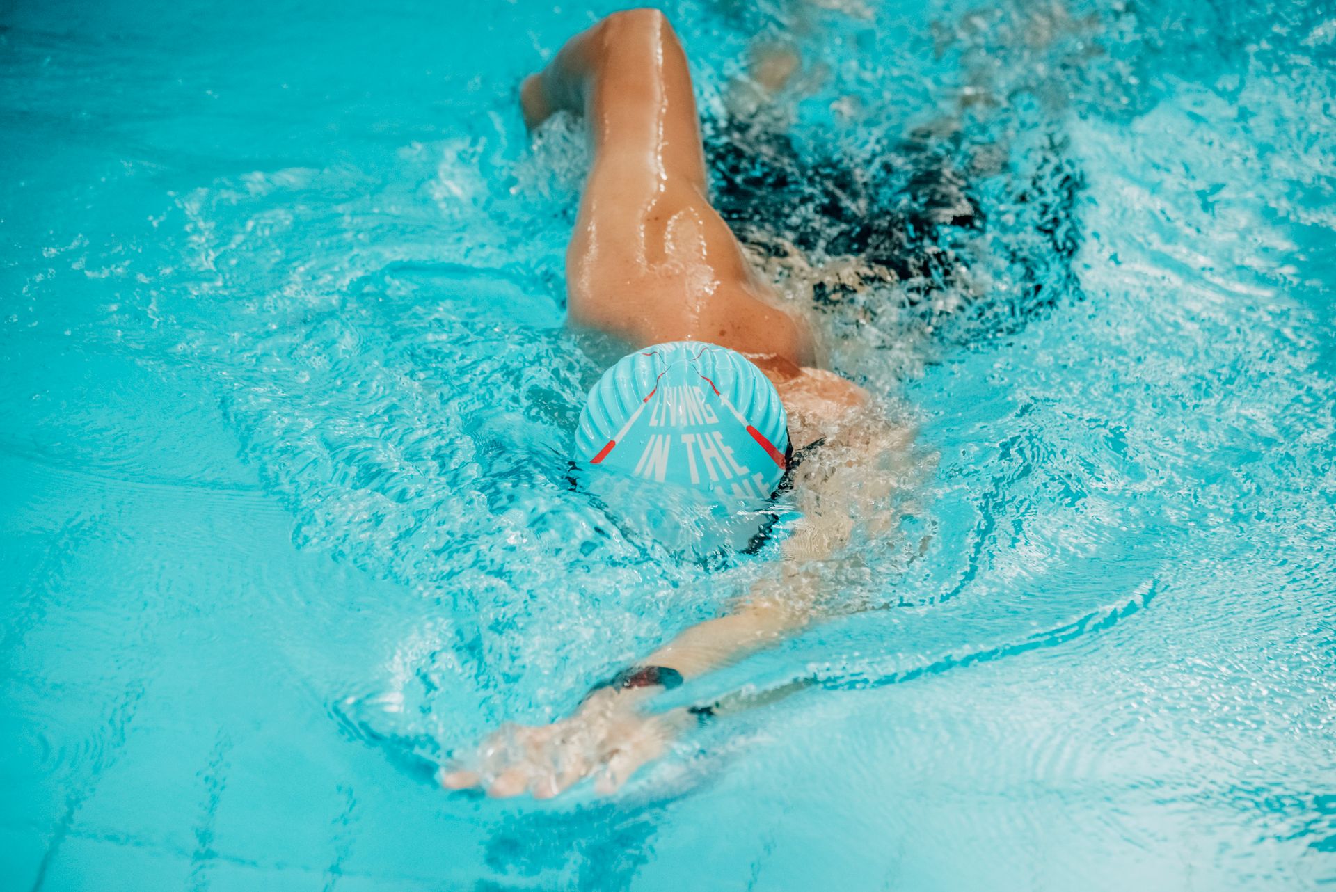 Adult swimmer doing freestyle stroke in a clear blue pool, showing athletic form and movement.