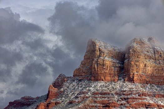 Dramatic winter scene of Sedona's snow-dusted red rock formations with looming clouds.