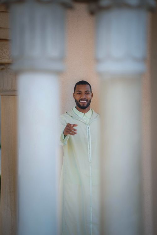 Free Smiling man in white traditional robe framed by classical columns, Casablanca. Stock Photo