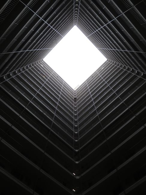 Upward view of modern skyscraper atrium leading to the sky, showcasing urban architecture.