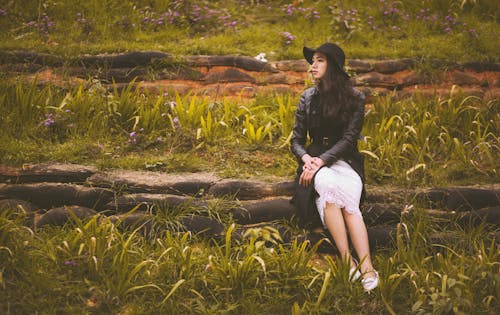 女人坐在綠草附近的灰色石屏障