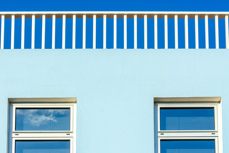 Capture of a modern facade with a white railing and blue wall reflecting the clear sky.