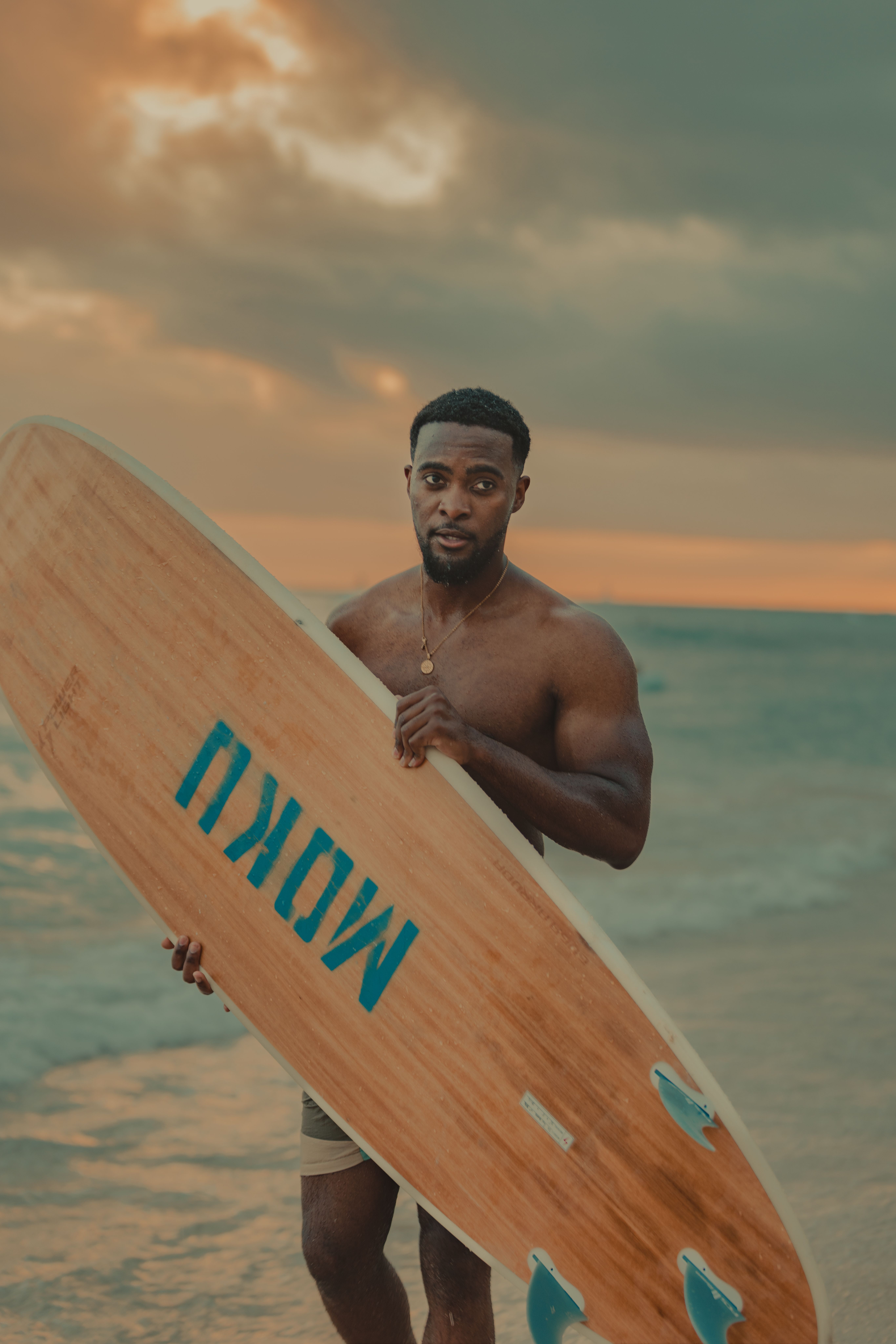 Man with surfboard on beach at sunset, embracing the ocean view.