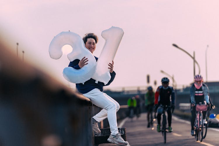 Person Posing With Birthday Balloons And People Cycling Near