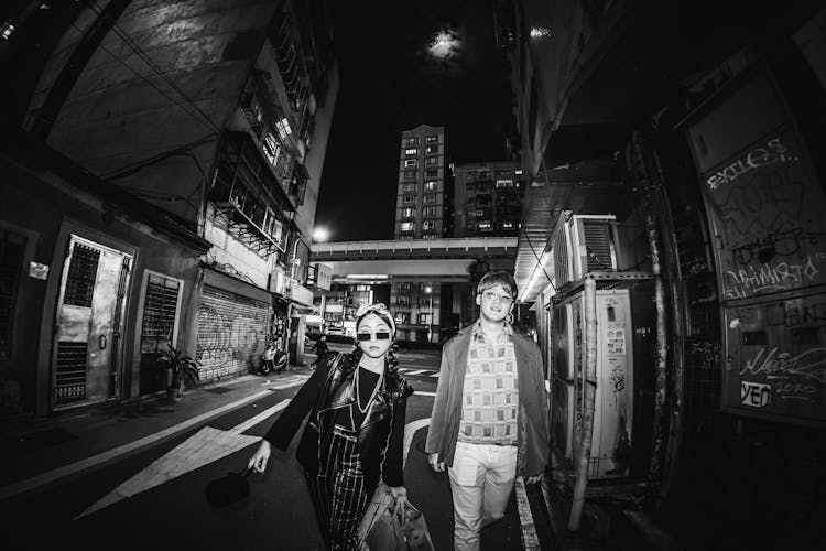 Black And White Photo Of A Young Man And Woman Walking On The Street At Night