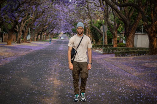 A Man Standing on a Street between Trees with Purple Flowers