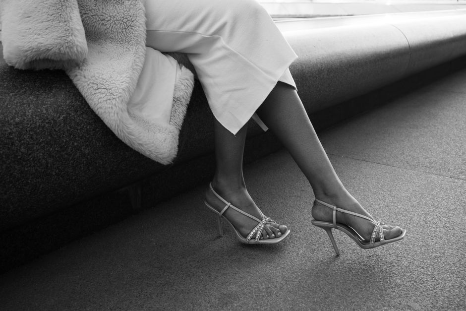 A stylish woman in high heels sits gracefully on a concrete bench, exuding elegance and sophistication.