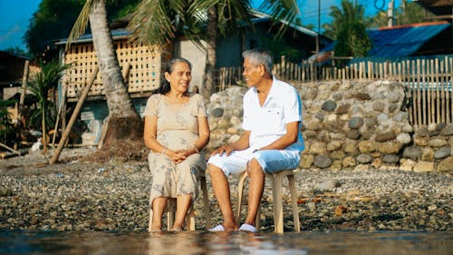 Senior Couple Sitting on Pebbled Beach Wetting Their Feet