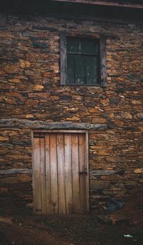 Weathered door and window on a rustic stone house wall, evoking rural charm and history.