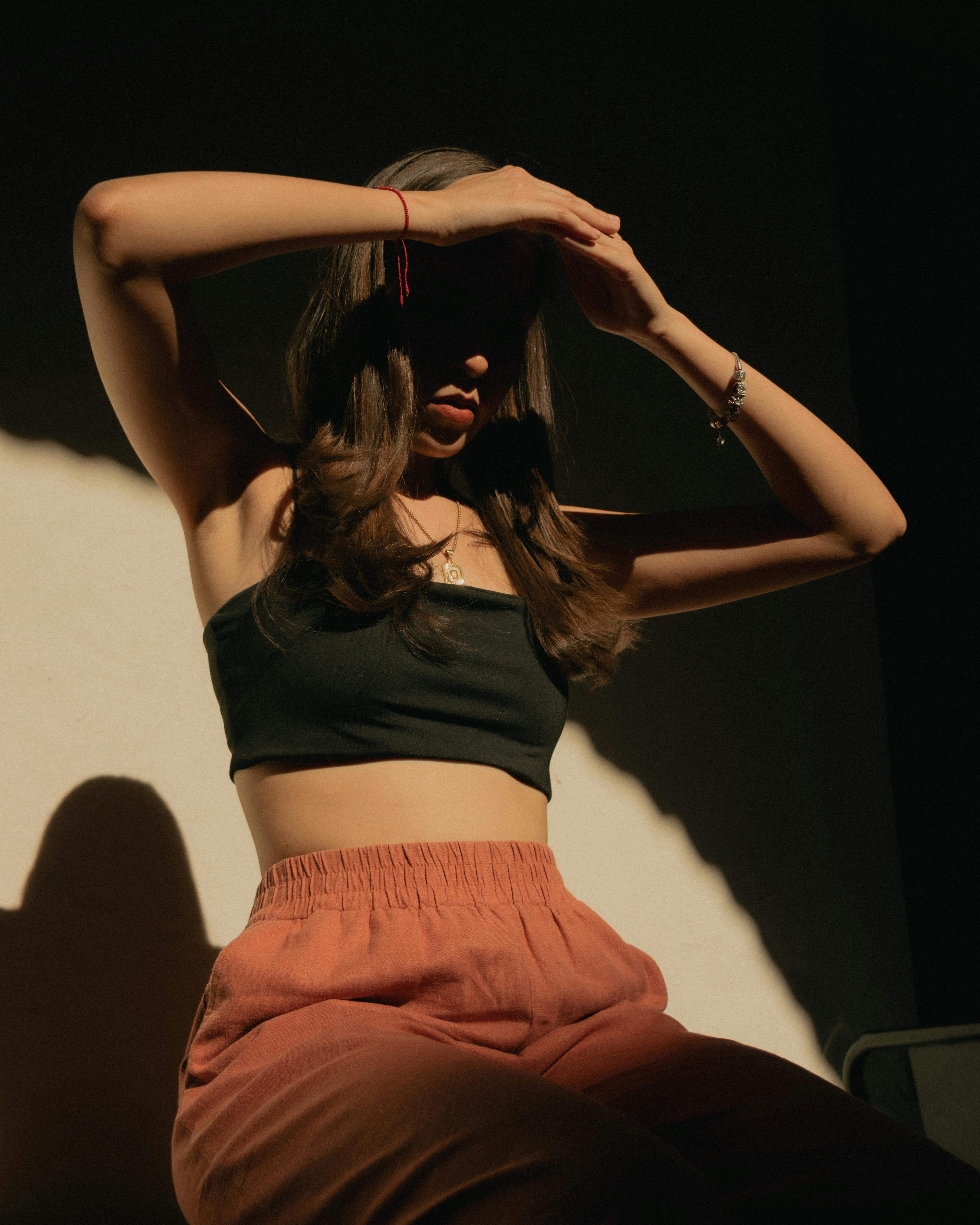 Artistic fashion portrait of a young woman with long hair in warm sunlight, posing with her hands up.