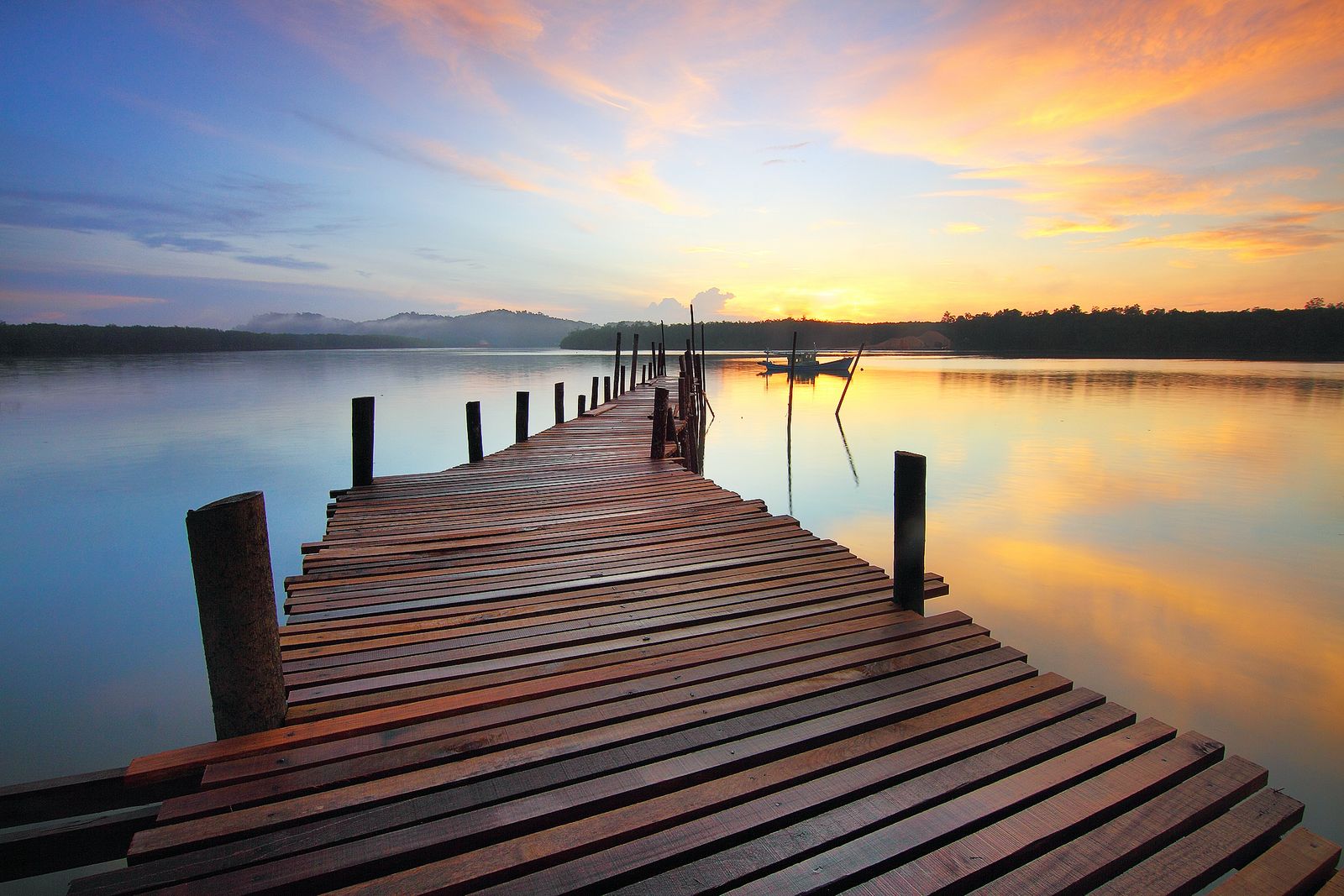 A wooden dock reaching into a calm lake at golden sunset