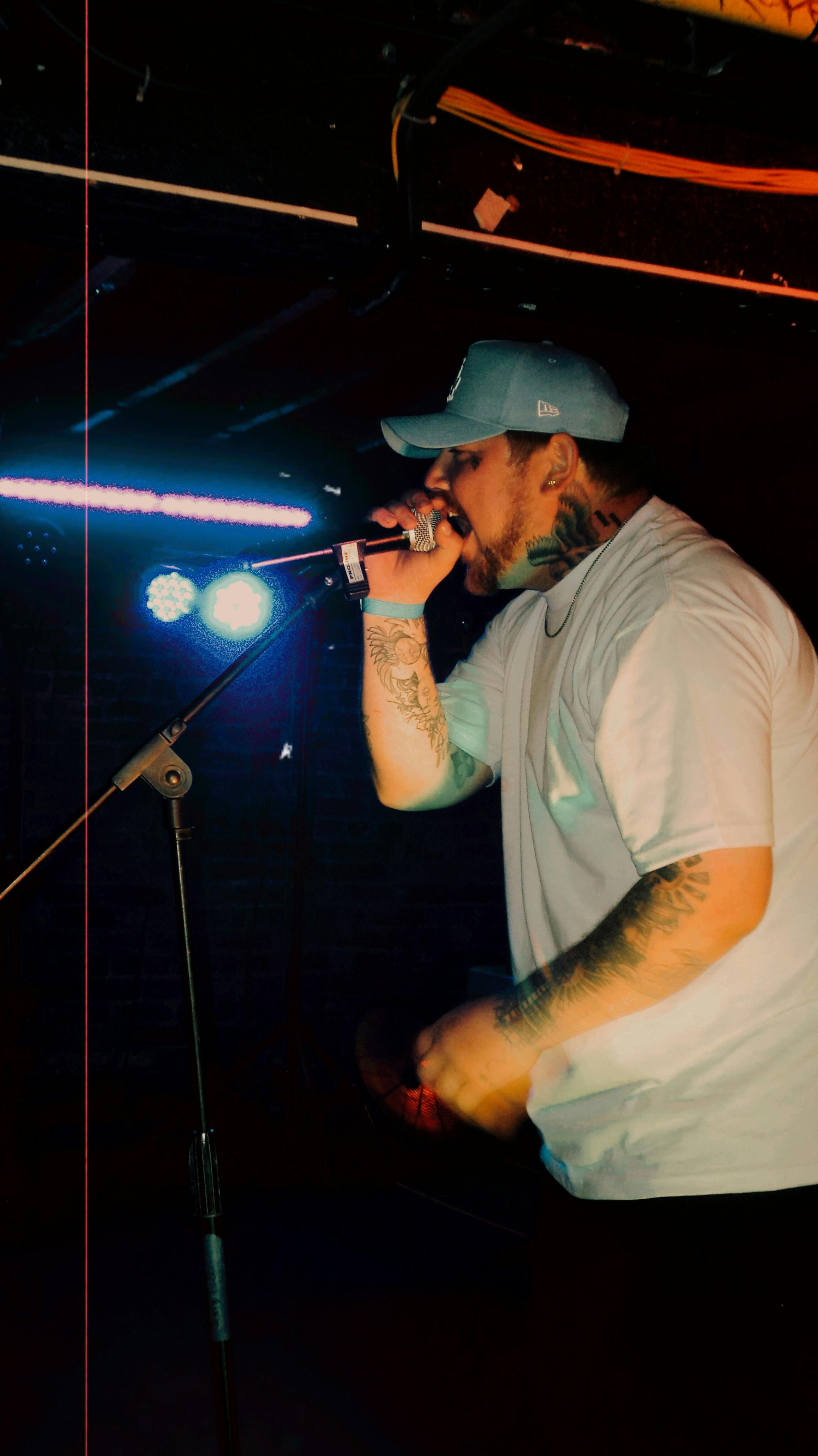 Dynamic image of a tattooed rapper passionately performing on stage under colorful stage lights.