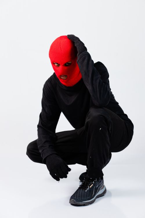 Free Stylized fashion portrait of a model in a red balaclava crouching against a white studio backdrop. Stock Photo