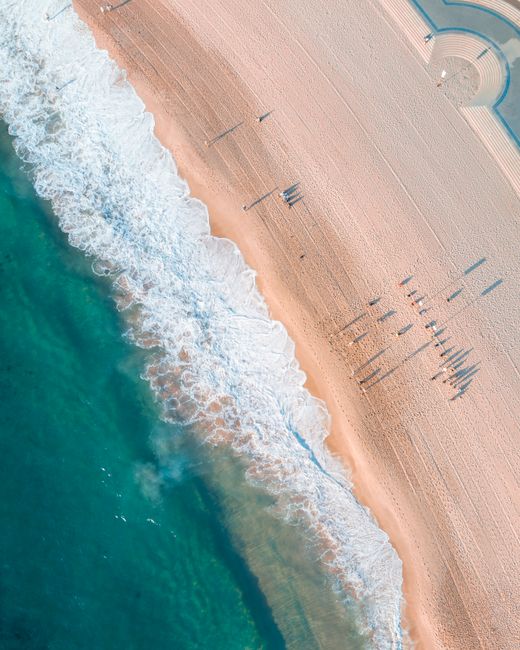 A breathtaking aerial shot showcasing clear ocean waves meeting a tranquil sandy beach under the bright sky.