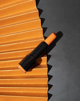 Orange lipstick on a pleated surface in artistic lighting, ideal for beauty ads.