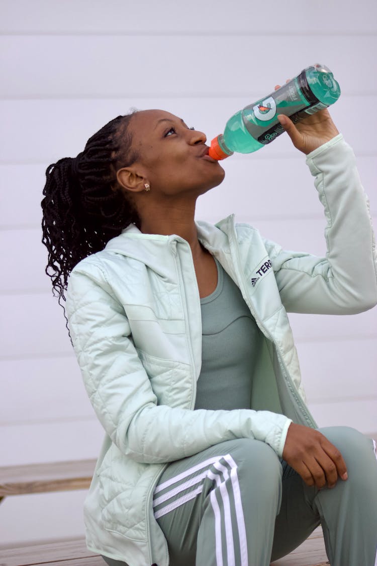 Woman In Sportswear Sitting And Drinking Water From A Bottle 