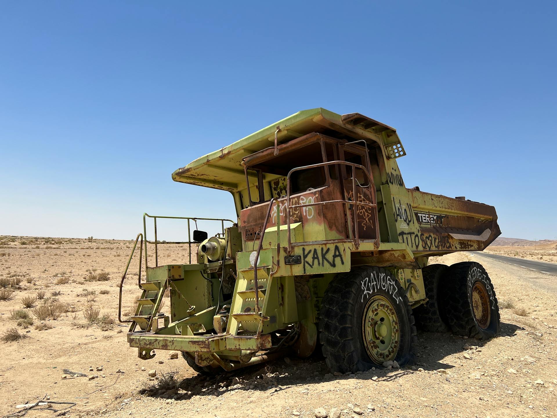 A rusty, abandoned mining dump truck stands in a barren desert landscape under a clear sky.