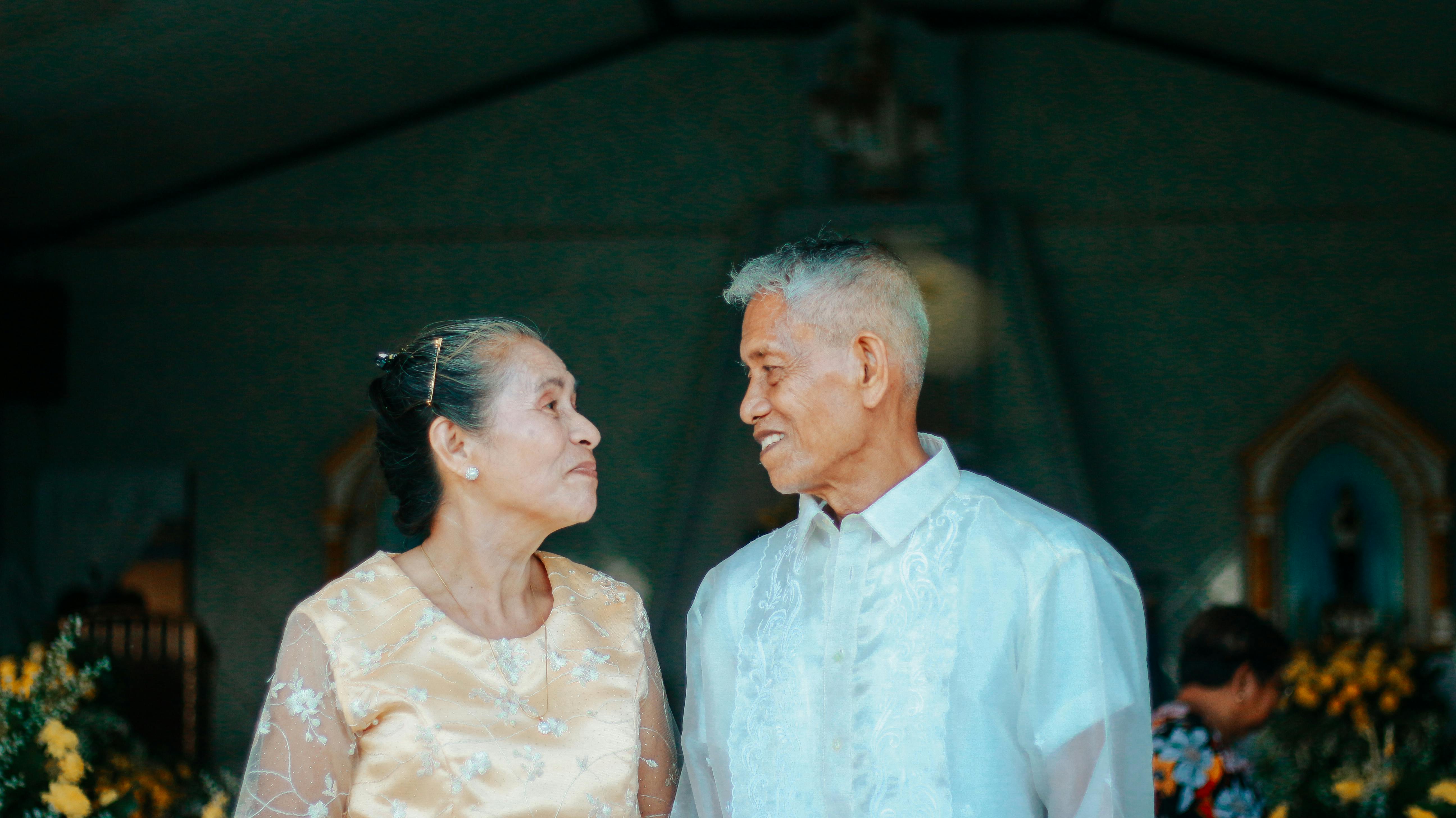 Elderly couple gazing at each other smiling, outside a church, with floral decorations.