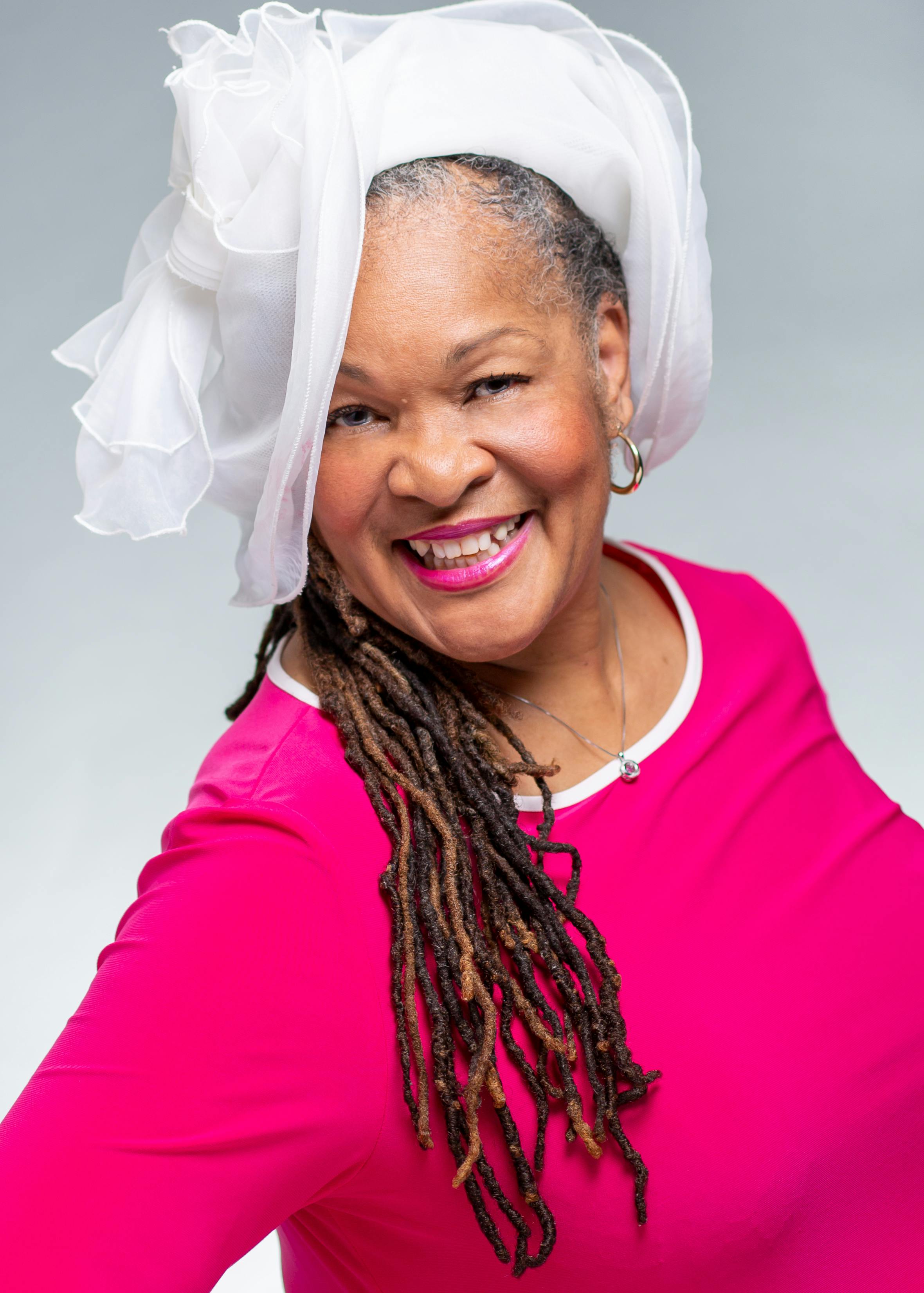 Portrait of a smiling mature woman in a pink blouse and elegant hat, exuding confidence.