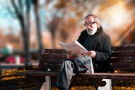 阳光明媚的公园里，一位留着胡子的老人正坐在木凳上看报纸