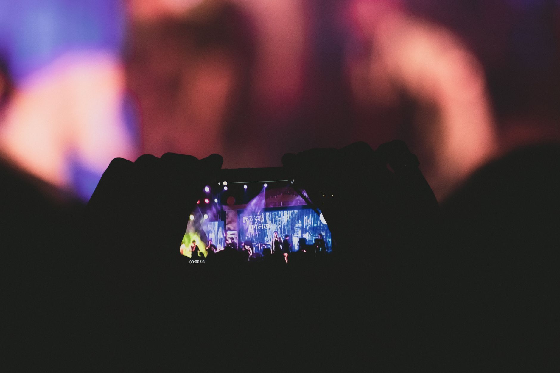 Silhouette of hands recording a vibrant concert scene with a smartphone.