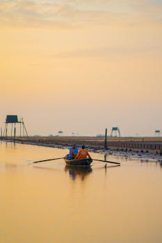 Two men rowing a boat at sunset in Thái Bình, Vietnam. Calm waters and vibrant sky.