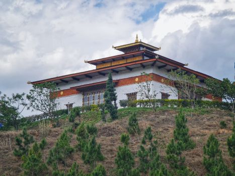 Elevated view of a traditional Bhutanese temple atop a green hillside under a cloudy sky in Wangdue Phodrang.