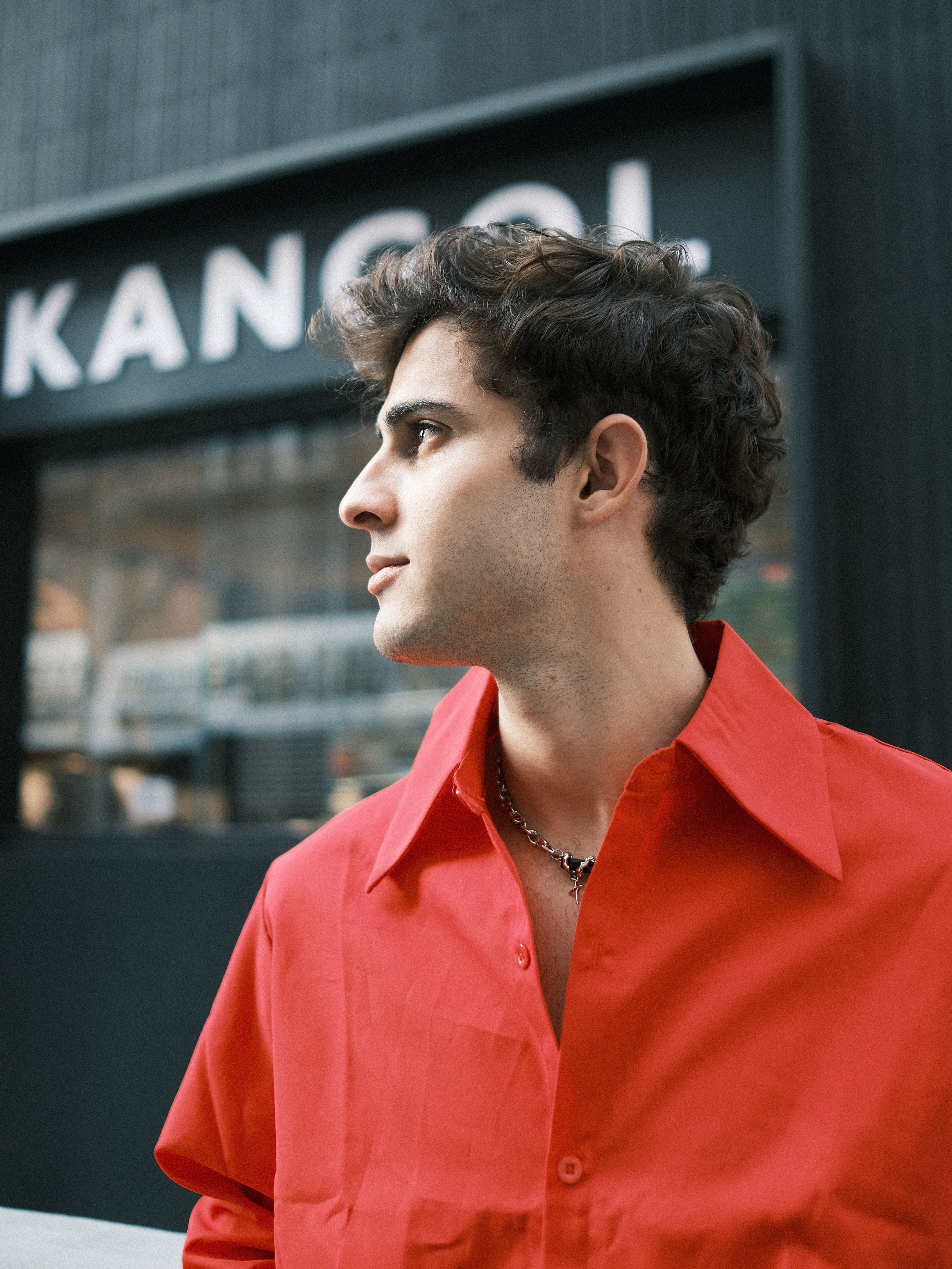 Stylish man in red shirt outdoors, showcasing modern fashion flair.