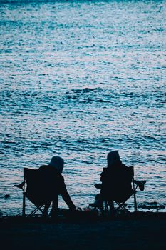Silhouettes of two people relaxing by the beach enjoying the calm sea view.