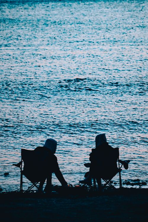 Free Silhouettes of two people relaxing by the beach enjoying the calm sea view. Stock Photo