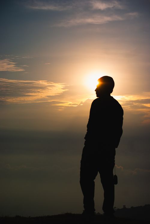 Free Silhouette of a man standing on a mountain peak during sunset, backlit by the sun. Stock Photo