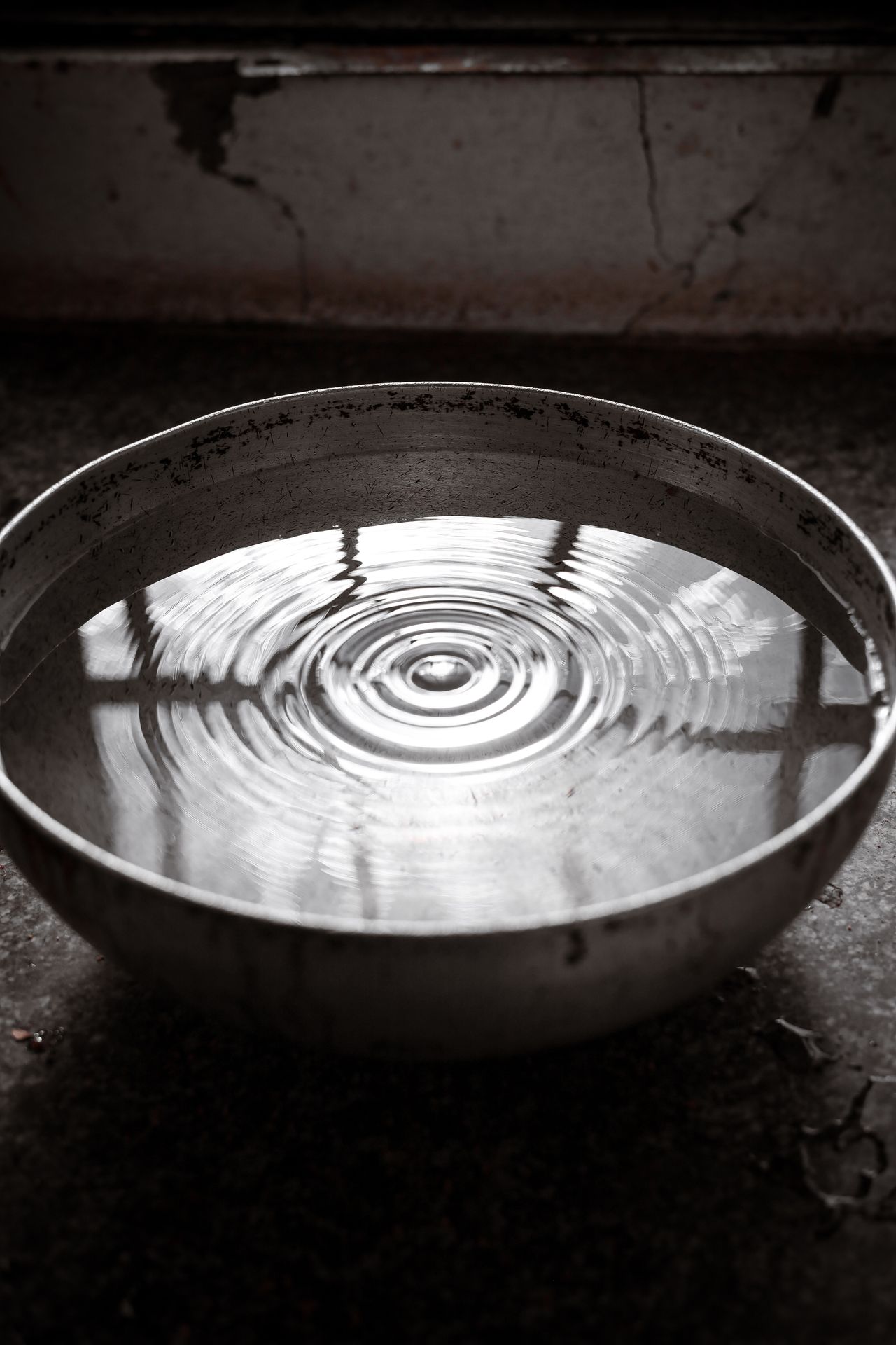 Ripples spreading across water in a large steel bowl, black and white