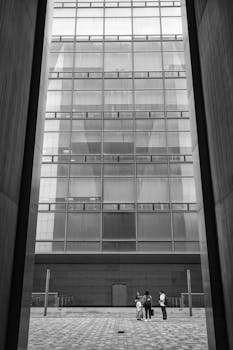 Black and white photo of people standing near a modern skyscraper in an urban environment.