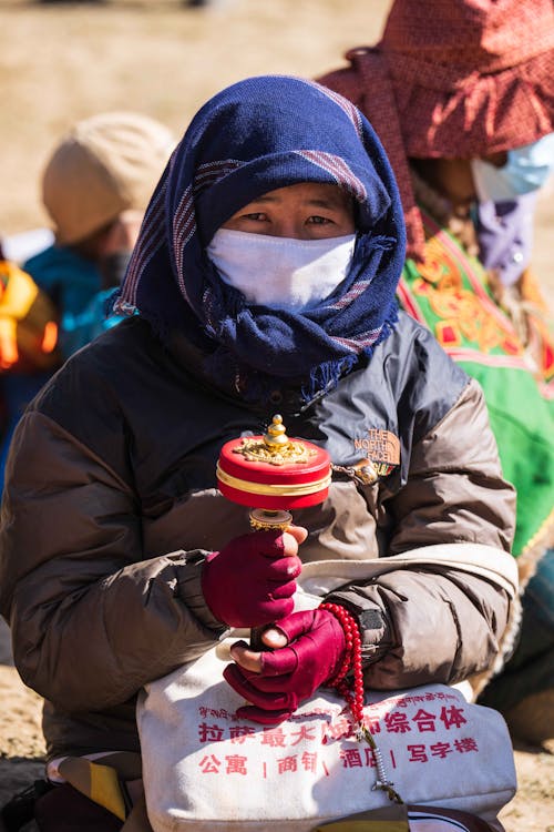 Woman in Mask and Shawl Holding Decorated Item