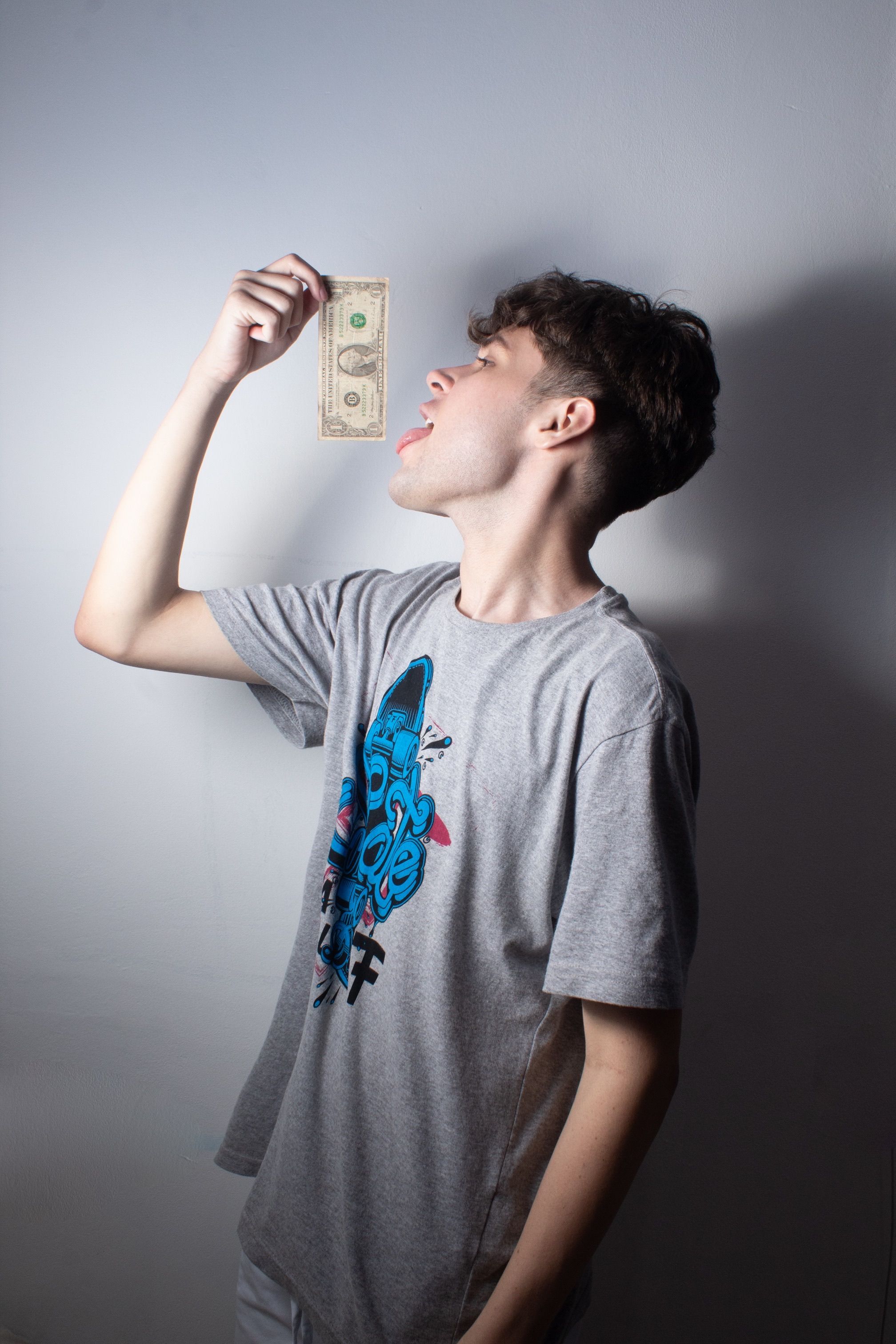A young man licking a dollar bill, showing greed. Studio shot on white background.