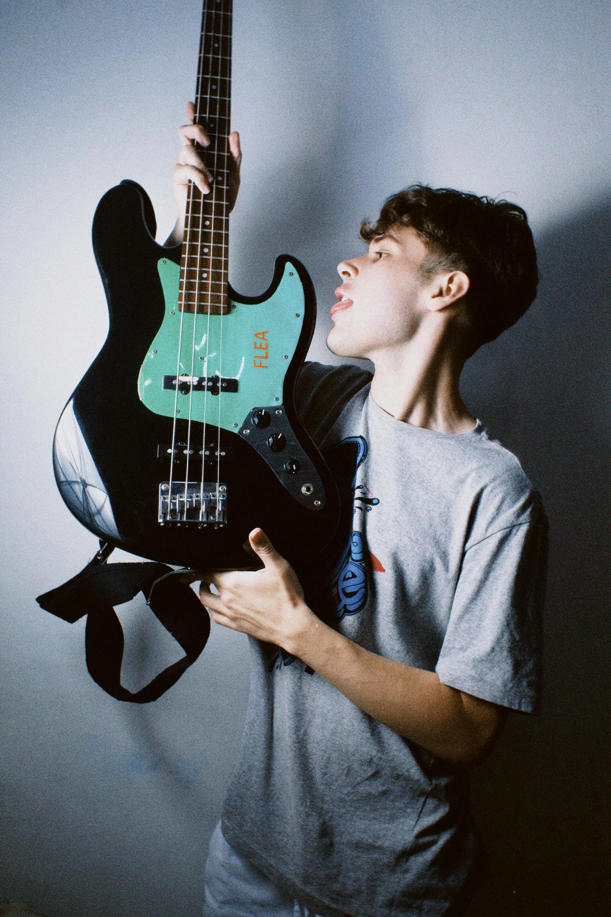 Portrait of a young man holding a bass guitar, posing creatively indoors with a cool vibe.