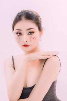 Portrait of a young woman with gem embellishments, stylish makeup, and pastel background.