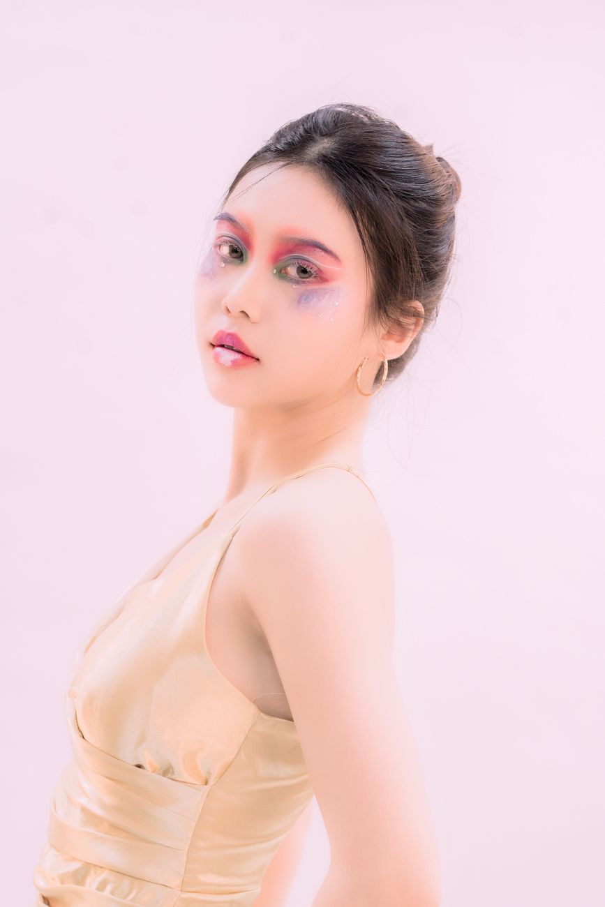 Artistic fashion portrait of a woman with vibrant makeup and elegant attire, featuring a soft white background.