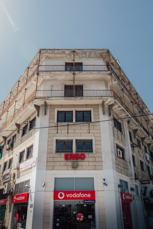 Free Photograph of a corner tenement with various storefronts including Vodafone and Ergo under a clear blue sky. Stock Photo
