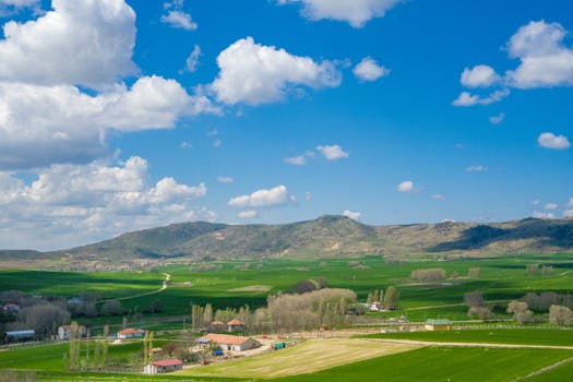 Stunning aerial view of a lush green countryside with a village and rolling hills under a vibrant blue sky.
